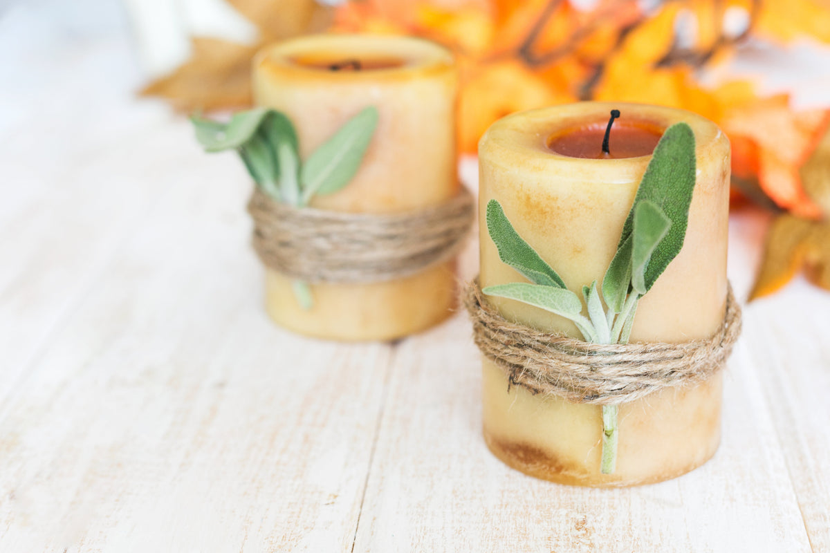 Two pillar candles wrapped in twine with sage